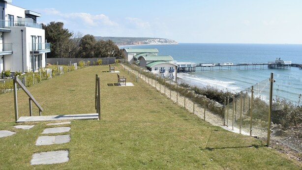Une propriété située en bord de mer, dotée d’une pelouse verdoyante, d’un chemin pavé, d’une jetée et offrant une vue sur la mer.