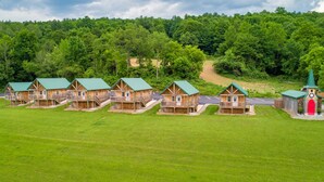 A row of wooden cabins with green roofs, set against a backdrop of dense forest and a winding road. - #4 Cabin, cottages, fishing, Hunting, Trails, nature, creek, ponds, lakes  (Oneida)