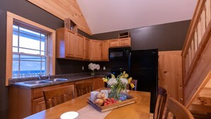 A kitchen with wooden cabinets, a black refrigerator, a microwave, and a dining table with a tray of food and flowers. - #4 Cabin, cottages, fishing, Hunting, Trails, nature, creek, ponds, lakes  (Oneida)