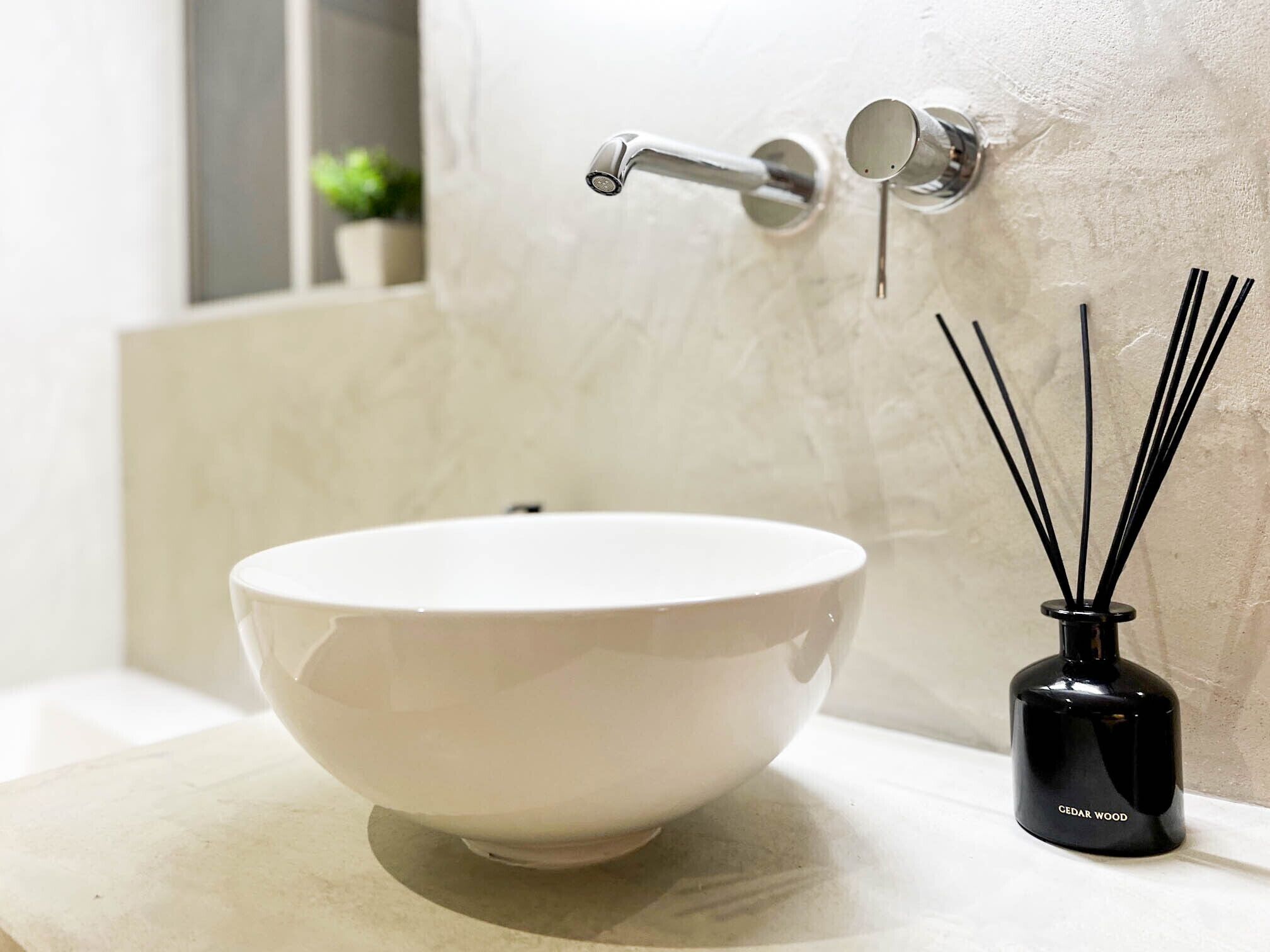 A white ceramic sink with a modern faucet, a black reed diffuser, and a marble wall.