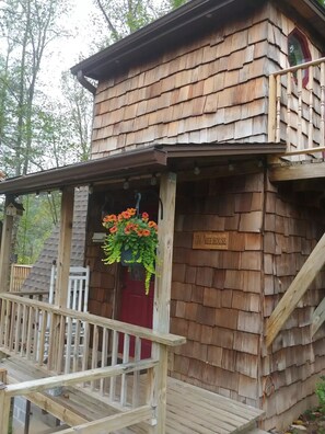 A wooden cabin with a porch, a red door, and a hanging flower basket. - Whee House (Cullowhee)
