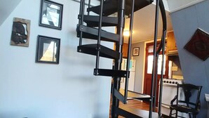 A modern living room with a spiral staircase, a sofa, a dining table, and a kitchen in the background. - Whee House (Cullowhee)
