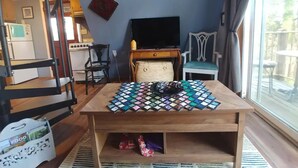 A cozy living room with a wooden coffee table, a television, and a dining area with chairs. - Whee House (Cullowhee)