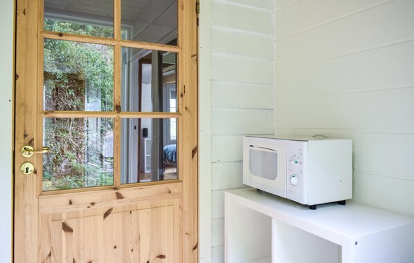 A wooden door with a glass panel, a white microwave on a white cabinet, and a view of greenery outside. - 2 bedroom beach front home in Vallavik (Vallavik)