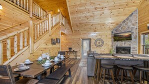 Un intérieur en bois comprenant un coin repas, des tabourets de bar, une cheminée en pierre et un escalier.