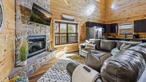 Un intérieur de chalet chaleureux avec une cheminée en pierre, un canapé en cuir et un coin cuisine.