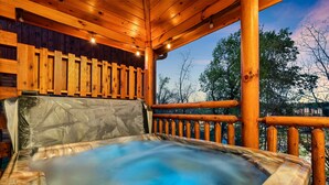 Une terrasse en bois avec un jacuzzi, des rampes en bois et une vue sur les arbres.