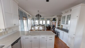 A spacious kitchen with white cabinetry, a central island, and a dining area with a chandelier. - High Tide - Beachfront Home in "Arrogantly Shabby" Pawleys Island, SC (Pawleys Island)