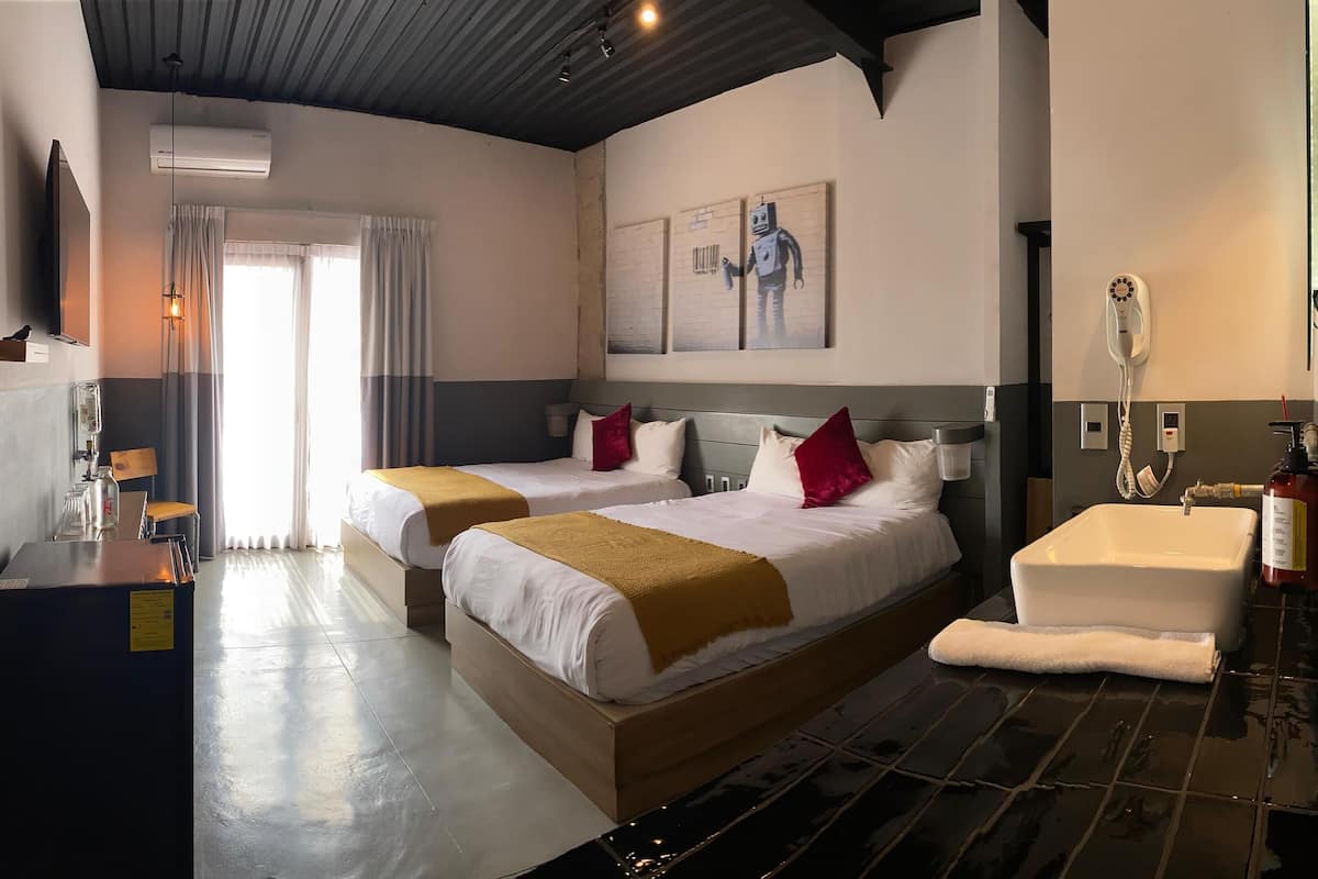 A hotel room with two beds, a large window, a sink, and a fire extinguisher.