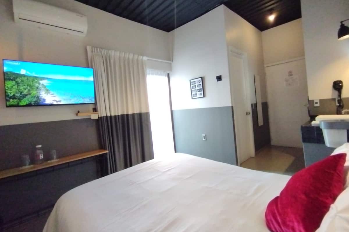A hotel room with a bed, a TV mounted on the wall, a door, and a small desk with a lamp.