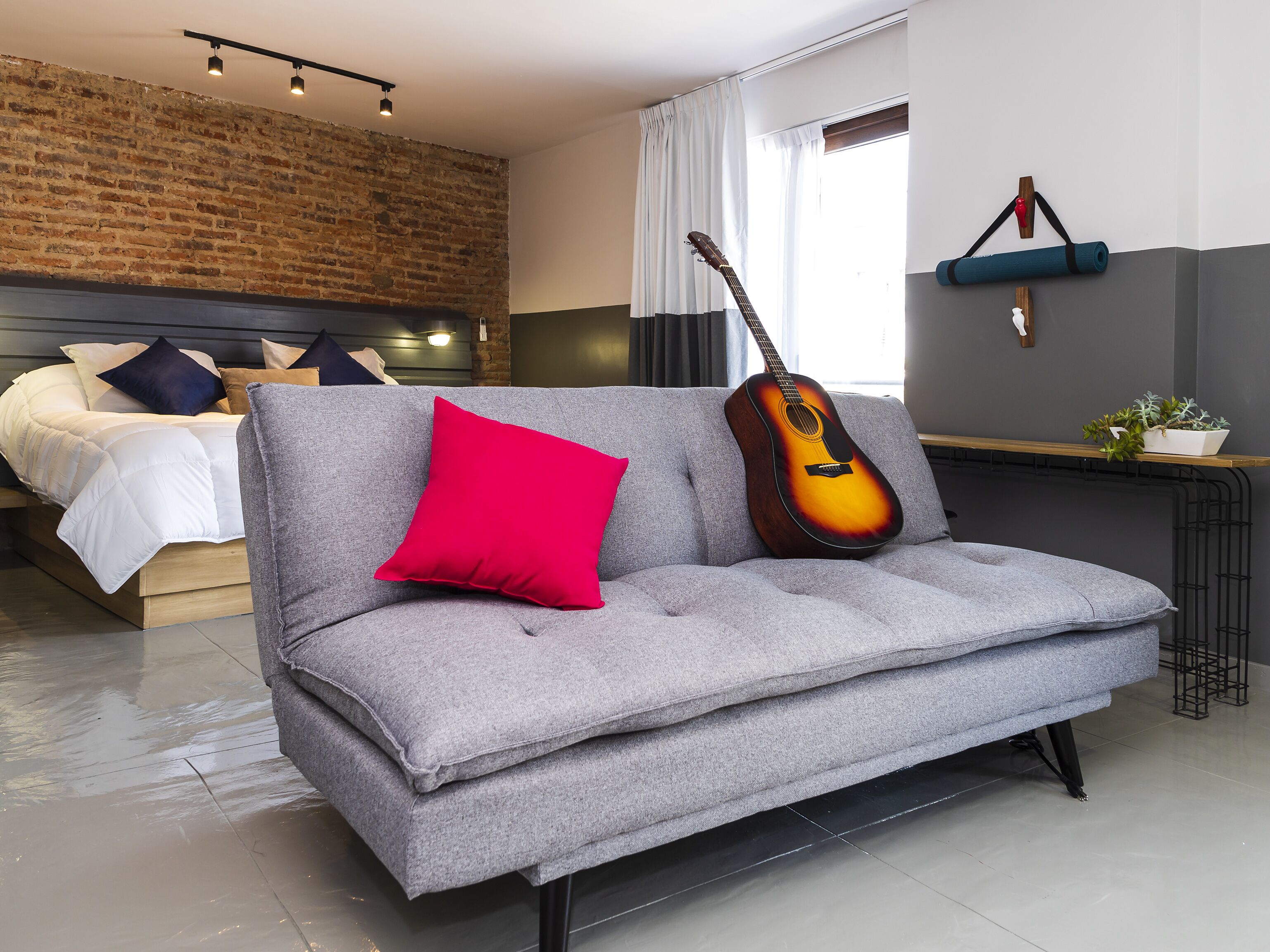 A modern living room with a grey sofa, a red pillow, and a guitar leaning against the wall.