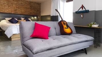A modern living room with a grey sofa, a red pillow, and a guitar leaning against the wall.