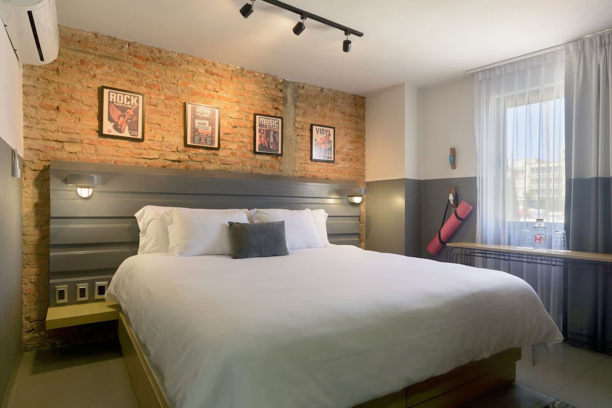 A bedroom with a brick wall, a bed with white bedding, and framed posters on the wall.