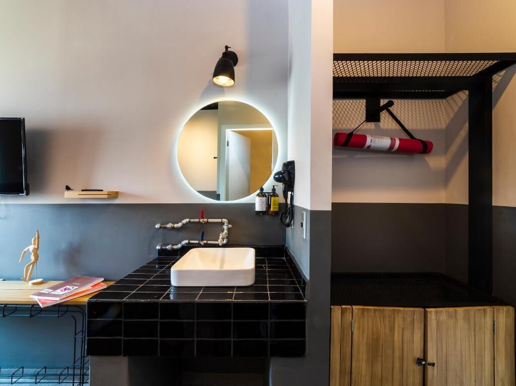 Une salle de bain moderne avec un comptoir recouvert de carreaux noirs, un lavabo blanc, un miroir rond avec éclairage intégré et un meuble en bois.