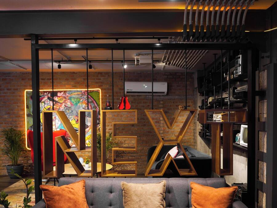 Un interior moderno con un letrero destacada de 'NEXI', una pared de ladrillo y una zona de estar con cojines.