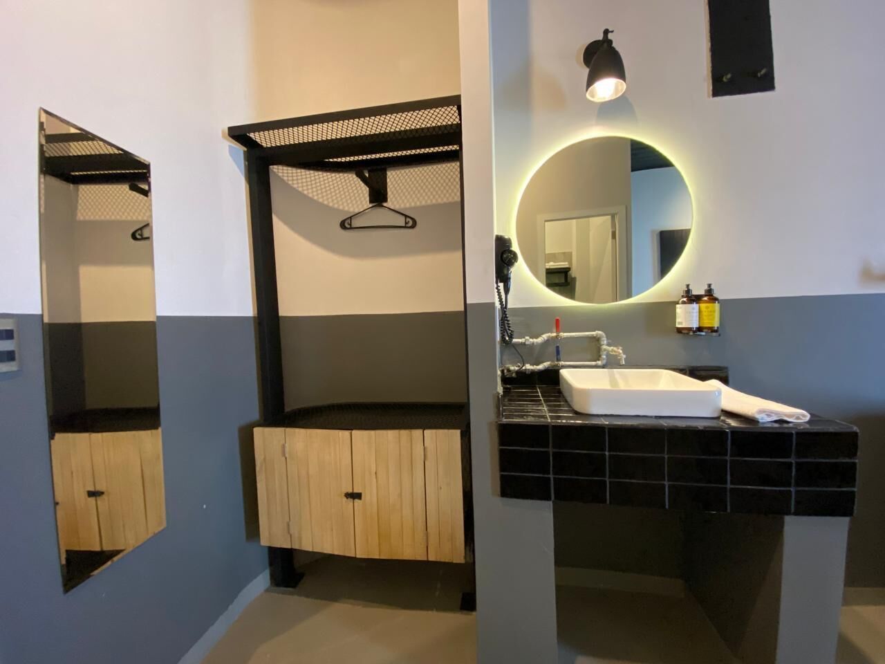 Ein modernes Badezimmer mit einem hölzernen Waschtisch, einem runden Spiegel mit Neonbeleuchtung und einer schwarzen Spülen-Ecke.