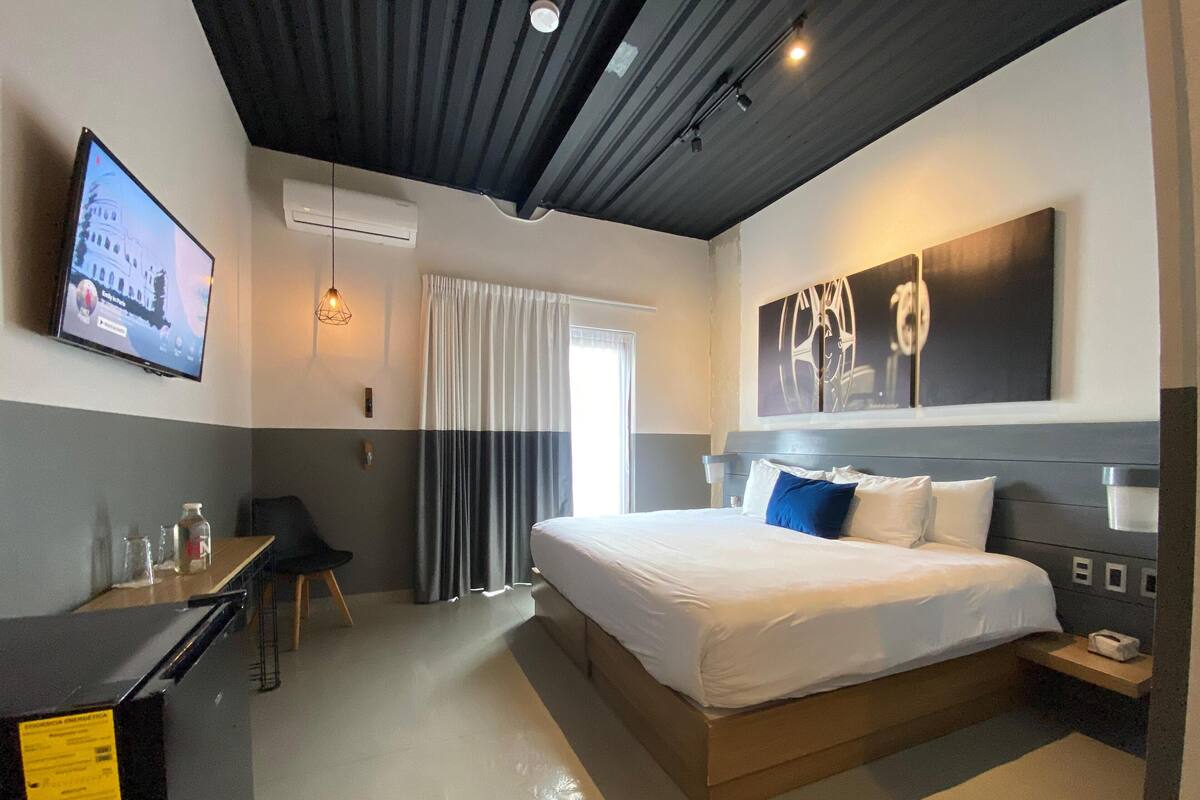 A modern hotel room with a large bed, a desk, a television, and a window with curtains.