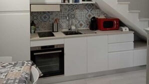 Une cuisine compacte avec des meubles blancs, un four encastré, un évier et un four à micro-ondes.