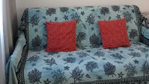 Un canapé bleu clair orné d’un motif de feuilles et agrémenté de deux coussins rouges. Un miroir décoratif, également orné d’un motif de feuilles, est accroché au mur au-dessus du canapé.