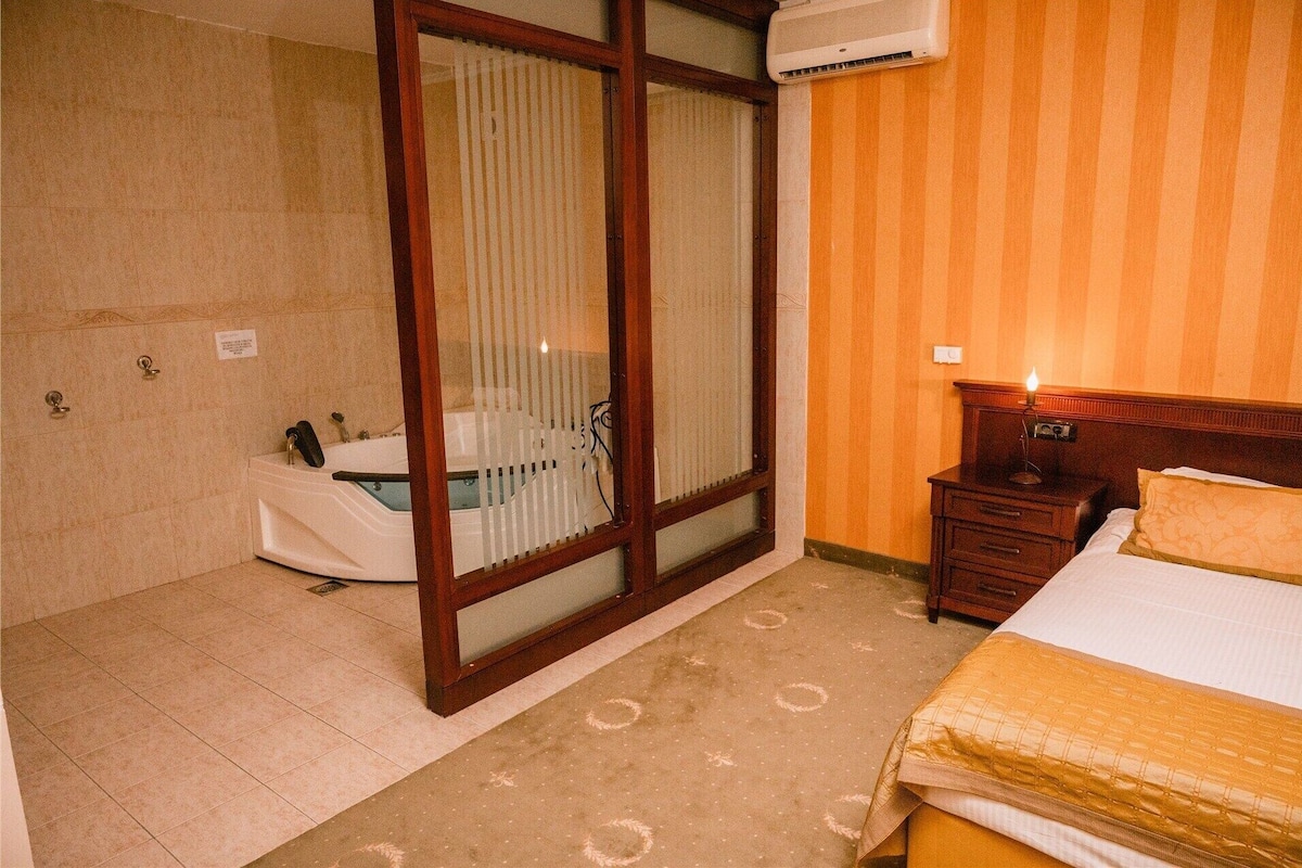 Une chambre d’hôtel avec une baignoire, une table de chevet en bois avec une lampe et un lit recouvert d’une couvre-lit à motifs.