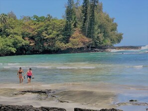 Une plage bordée d’une eau turquoise et limpide, d’un rivage rocheux et, en arrière-plan, d’une végétation luxuriante.