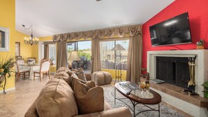 A living room with a sofa, a coffee table, a fireplace, and a TV mounted on the wall.