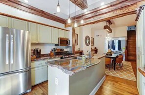 Una cocina moderna con electrodomésticos de acero inoxidable, una isla grande, vigas de madera y un comedor con mesa y sillas.