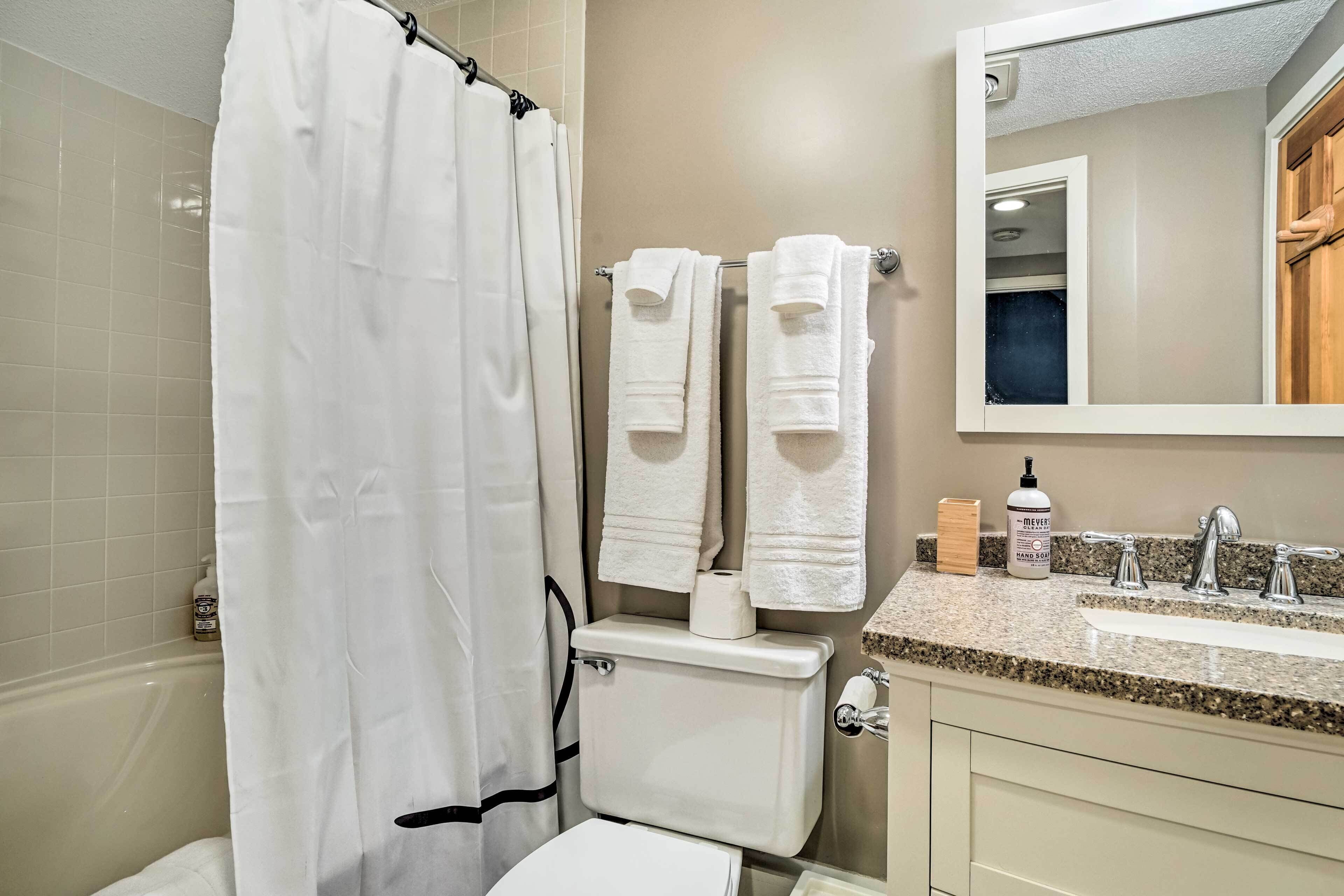 A bathroom with a shower curtain, two towels hanging on a rack, a toilet, a sink with a soap dispenser, and a mirror.