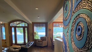 A spacious living room with a large window, a fireplace, and a modern art piece on the wall. - Bears Beach House (Tofino)