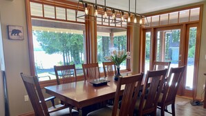 A dining area with a wooden table and chairs, large windows, and a hanging light fixture. - Bears Beach House (Tofino)