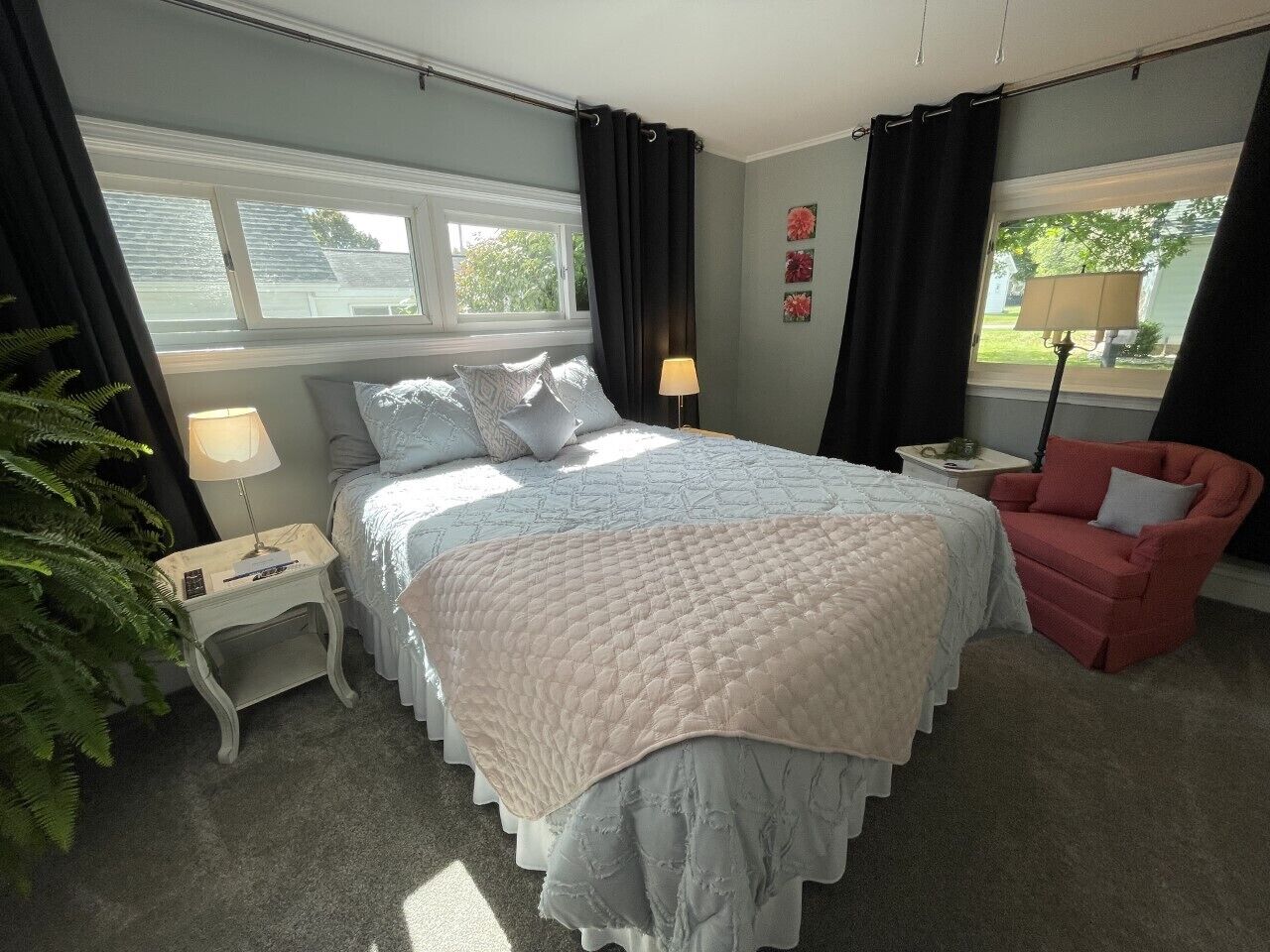 A bedroom with a large bed, a nightstand, a chair, and a window with curtains.