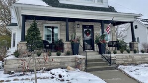 A two-story house with a front porch, a stone foundation, and a snow-covered roof. - Charming 1912 Bungalow in Middlebury Indiana (Middlebury)