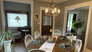 A dining room with a wooden table, white chairs, a chandelier, and a bowl of decorative items. - Charming 1912 Bungalow in Middlebury Indiana (Middlebury)