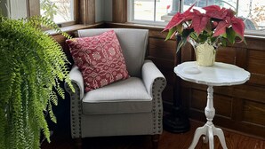 A corner room with a gray armchair, a small white table, a lamp, and a potted plant. - Charming 1912 Bungalow in Middlebury Indiana (Middlebury)