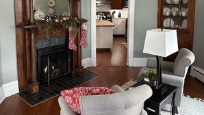A living room with a fireplace, a dining area, and a kitchen in the background. - Charming 1912 Bungalow in Middlebury Indiana (Middlebury)