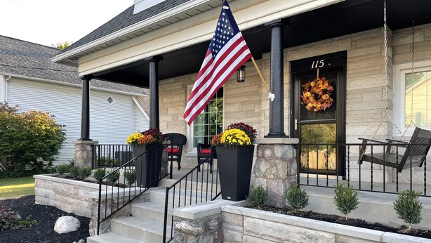 A house with a stone facade, a front porch with a flag, and a garage door number 115. - Charming 1912 Bungalow in Middlebury Indiana (Middlebury)