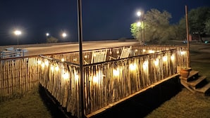 Un espacio al aire libre de noche con valla de bambú, farolas y vista despejada de la calle.