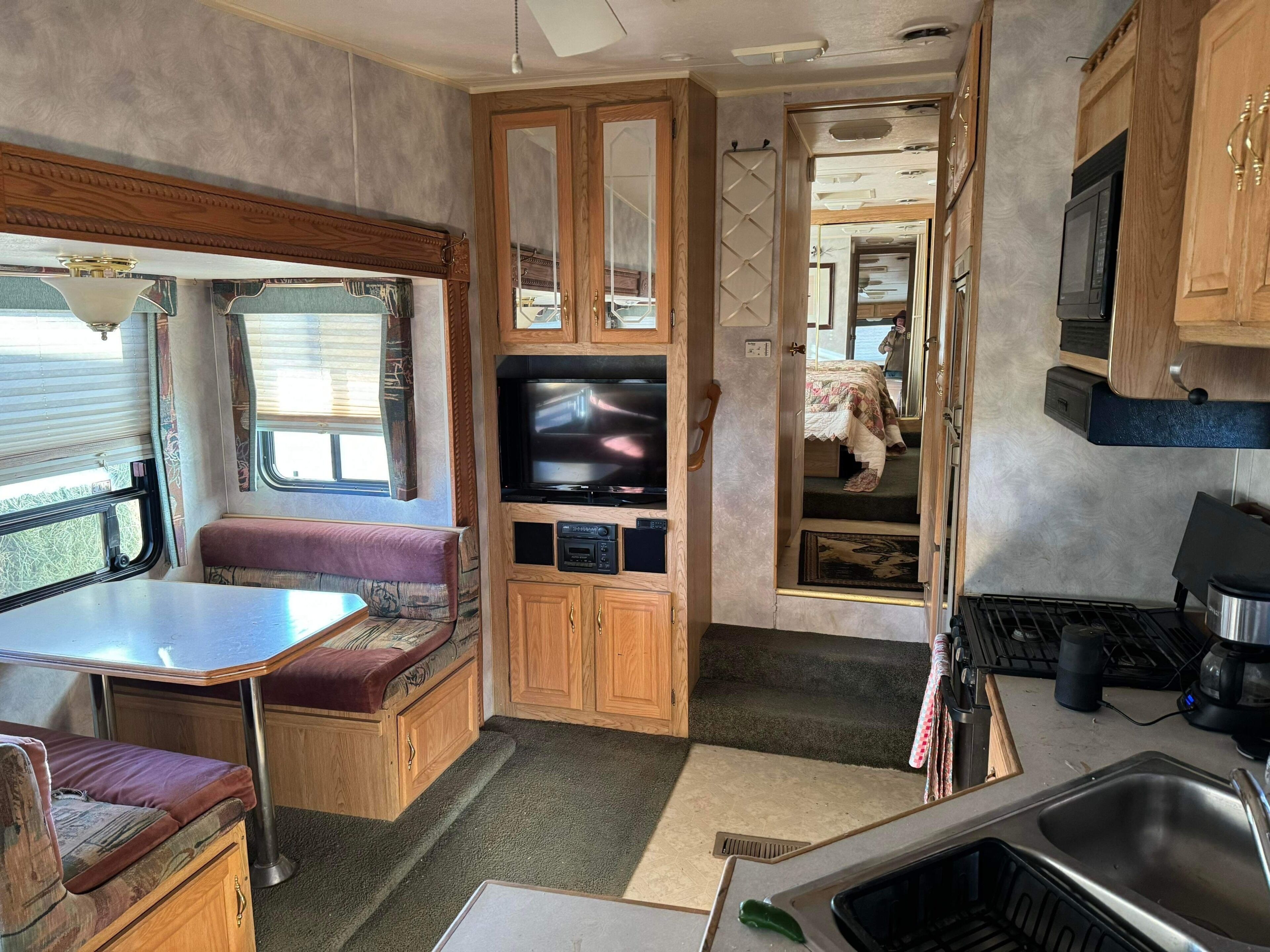 A compact RV interior with a kitchenette, a seating area, and a television.