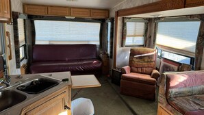 Ein Wohnmobil-Innenraum mit einer Küchenzeile, einer Couch, einem Sessel und einem Fenster.