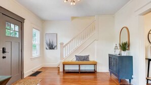 A spacious hallway with hardwood floors, a bench, a staircase, and a blue cabinet. - Completely Updated Home-sleeps 6-Centrally Located (Cincinnati)