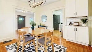 A dining area with a wooden table and chairs, a black and white rug, and a hanging light fixture. - Completely Updated Home-sleeps 6-Centrally Located (Cincinnati)