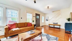 A spacious living room with a wooden floor, a sofa, a coffee table, and a staircase. - Completely Updated Home-sleeps 6-Centrally Located (Cincinnati)