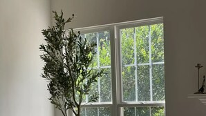 A room with a large window, a potted plant, and a wooden cabinet.