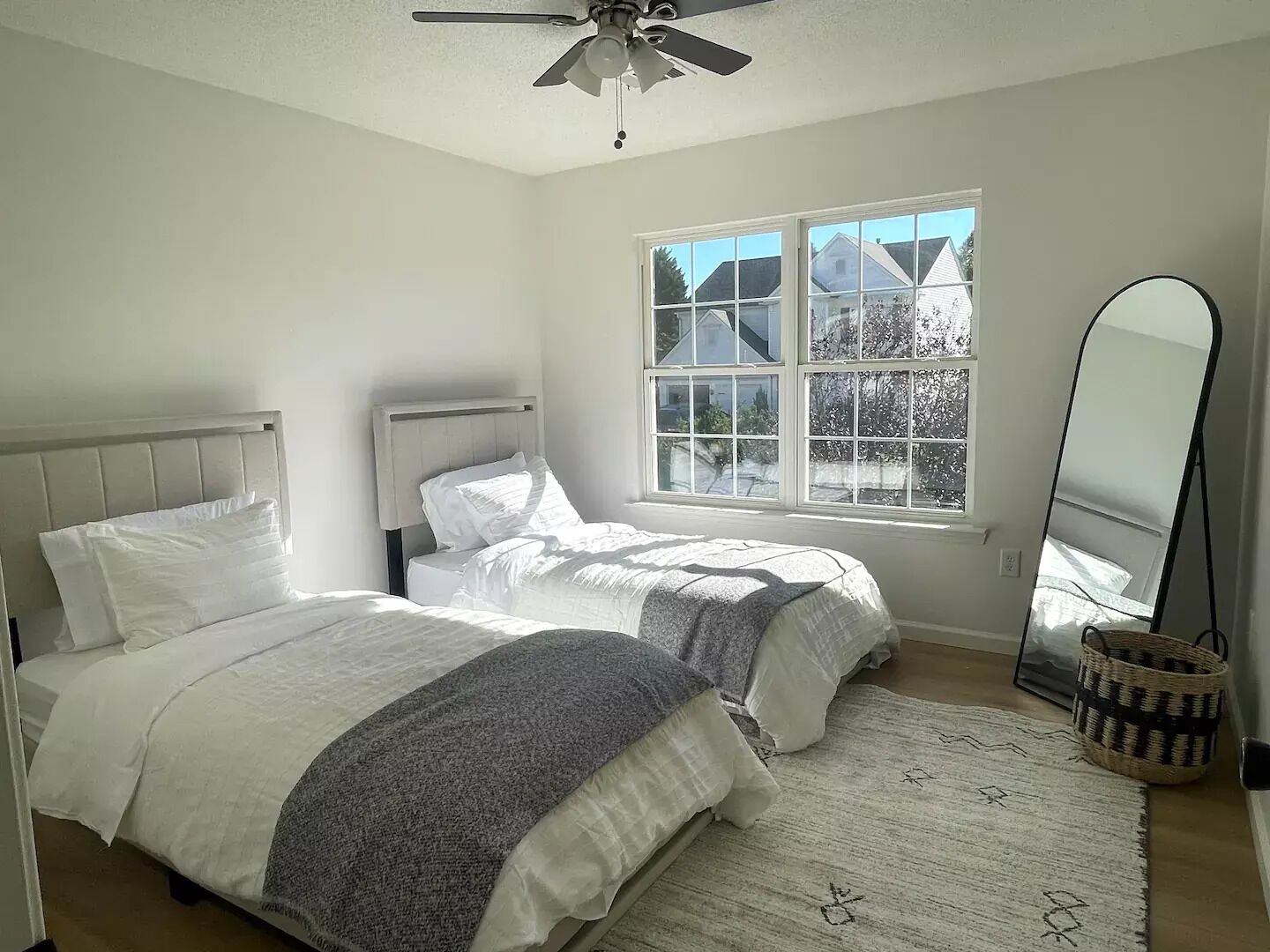 Ein Schlafzimmer mit zwei Betten, einem Deckenventilator, einem großen Fenster und einem Spiegel.