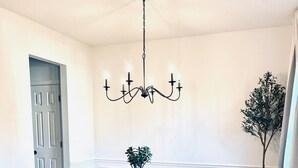 A dining room with a wooden table, six chairs, a chandelier, a potted plant, and a door.