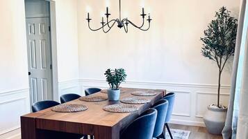 Une salle à manger avec une table en bois, six chaises, un lustre, une plante en pot et une porte.
