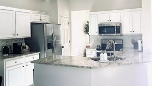 A modern kitchen with white cabinetry, a large island, stainless steel appliances, and a tiled floor.