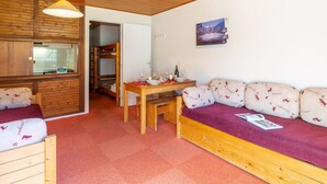 Une pièce chaleureuse avec un lit superposé en bois, une table à manger avec des chaises et un canapé agrémenté de coussins à motifs.