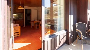 Un intérieur en bois comprenant un coin repas, une chaise en osier et une vue à travers une porte vitrée.