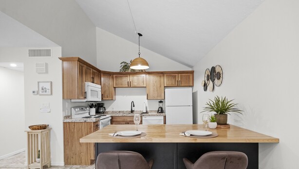 A modern kitchen with wooden cabinets, a central island with bar stools, a hanging pendant light, and a potted plant. - Updated condo with pools near golf courses (St. George)